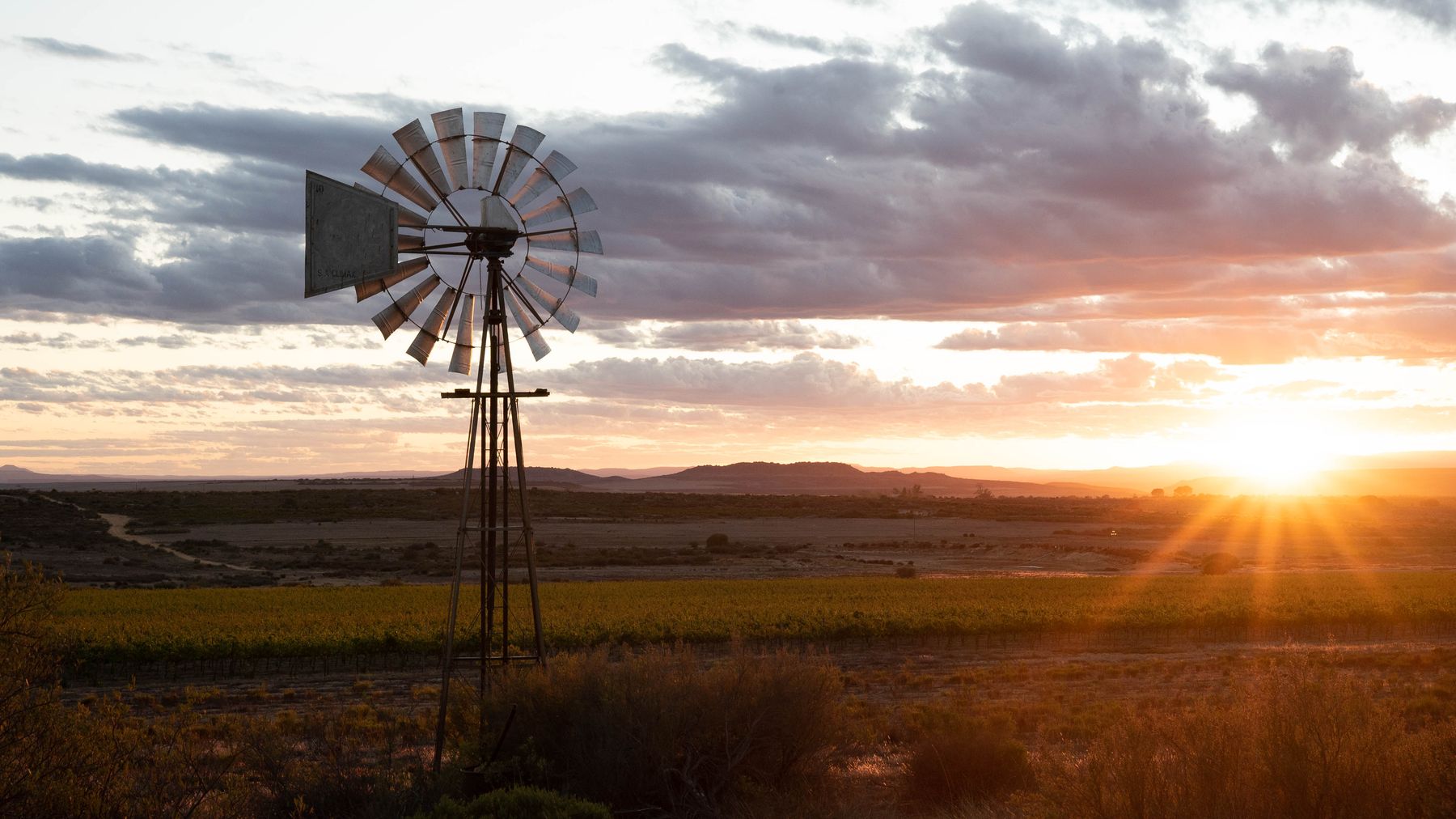 A windpump silhouetted against a sunset over flat Bokkeveld farmland